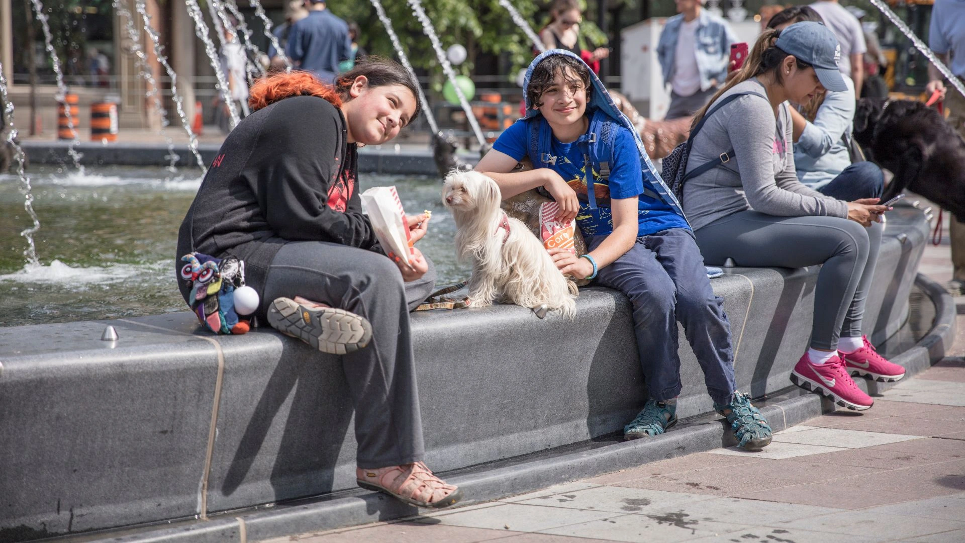 Children and dogs sitting on the rim of the granite water fountain in Berczy Park